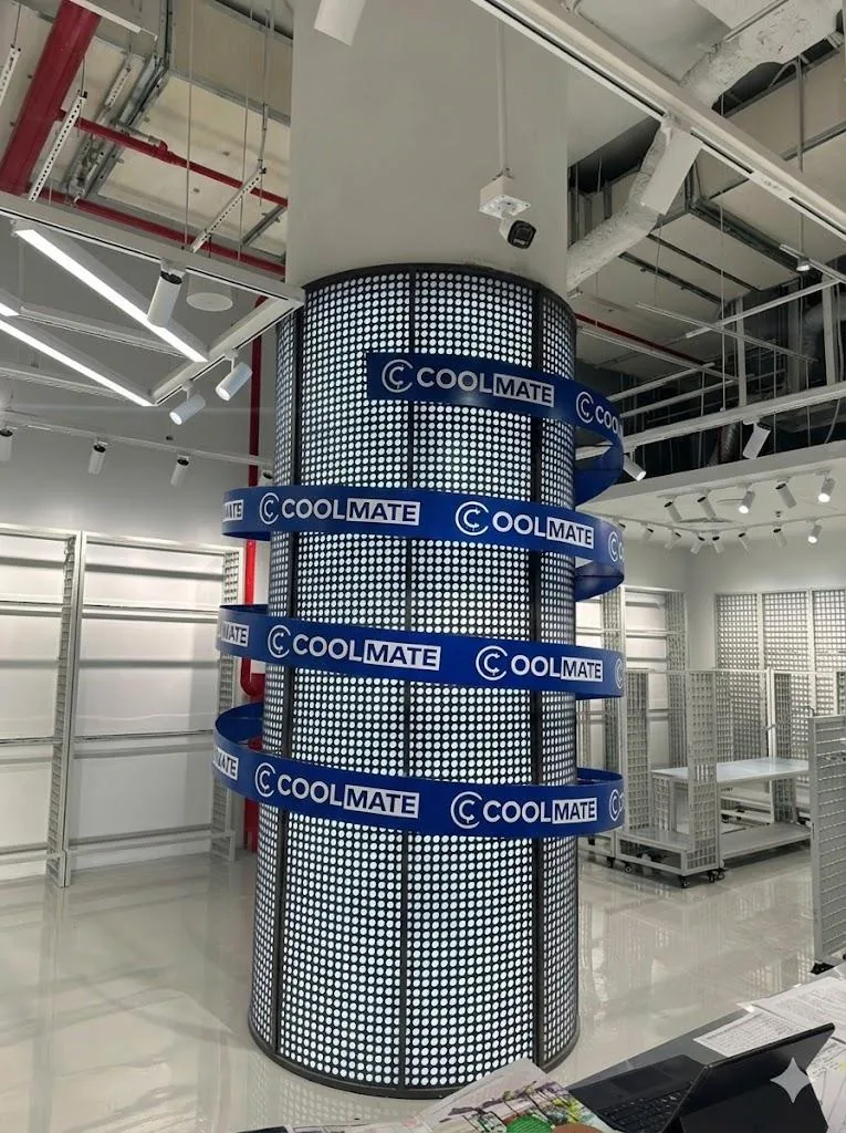 Hiện trạng cột trụ tròn tại cửa hàng Coolmate trước khi lắp LED dẻo: thân cột ốp tấm thép, ba vòng decal in tĩnh chữ COOLMATE màu xanh